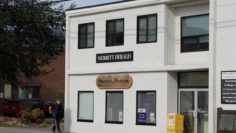 White building with the sign "the Merritt Herald" and a yellow newspaper box.