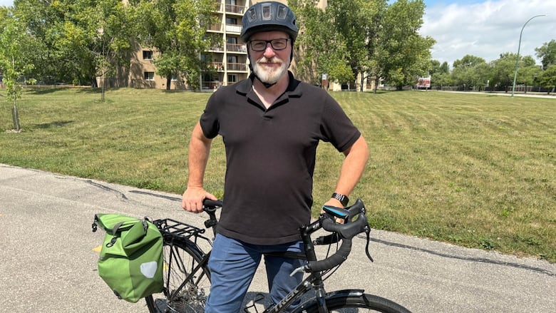 A man in a black shirt stands poses with a black bike. 