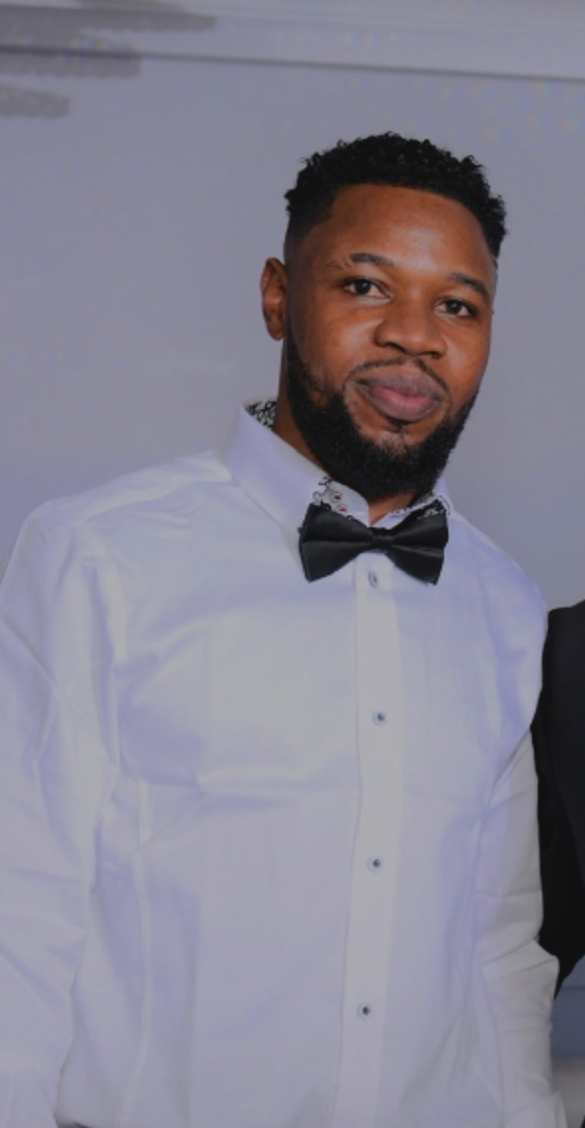 A Black man wearing a bow tie and white shirt smiles.