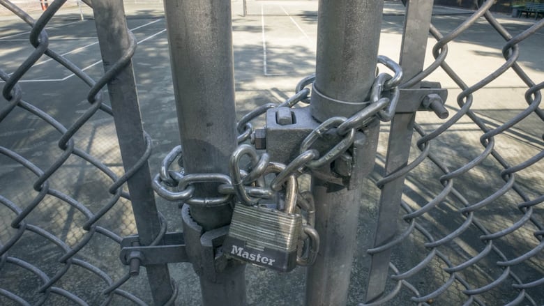 A padlock keeping the gates of a green tennis court shut. 