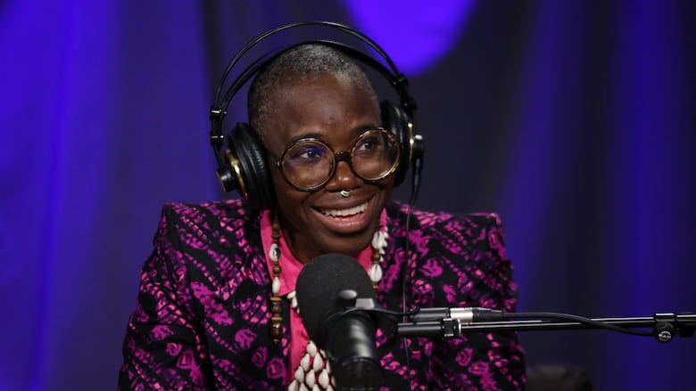A smiling woman wearing headphones sits in front of a studio microphone.