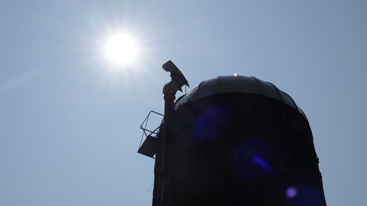 The sun shines in a clear blue sky next to a farm silo.