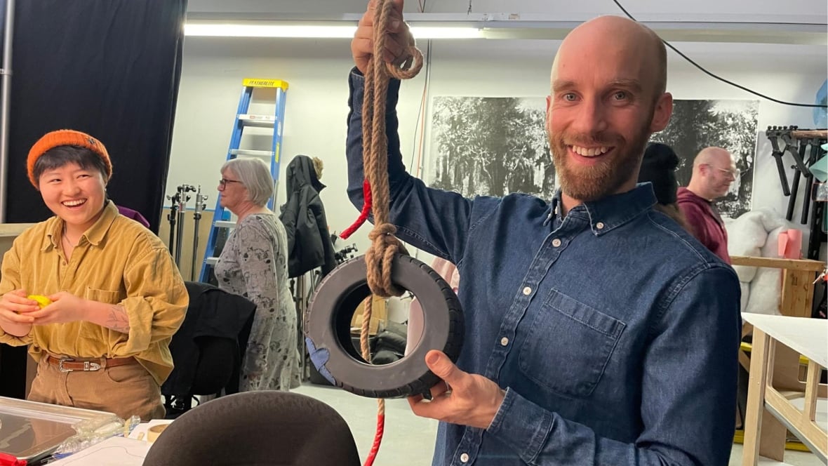 A smiling person holds up a model of a tire swing. 