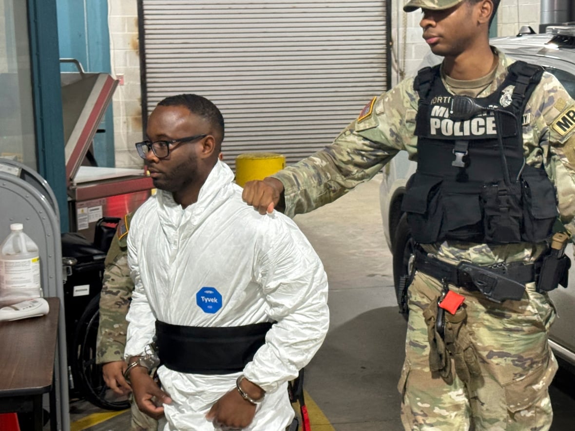 A dark-complected person in glasses and scrubs is led by a dark-complected military officer during a walk.