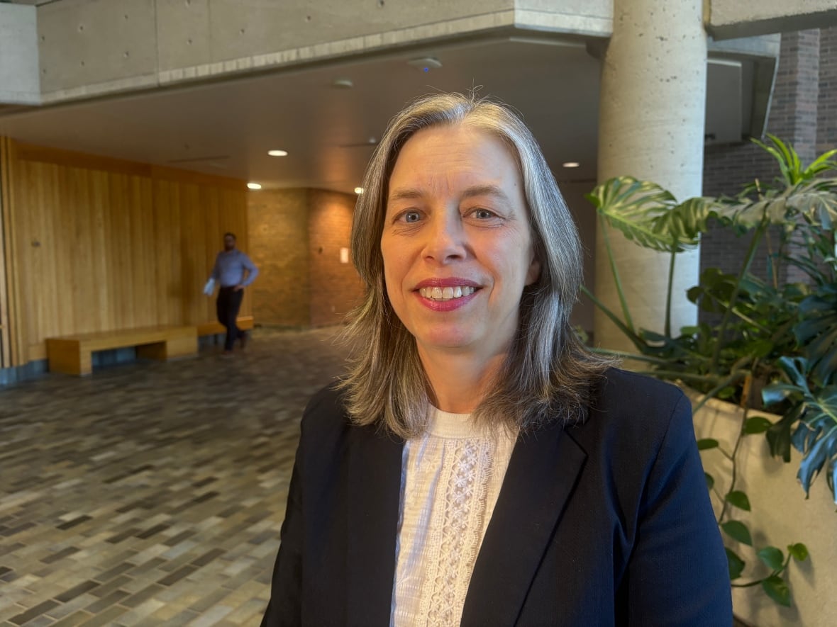 A smiling woman stands in the lobby of a building next to a plant.