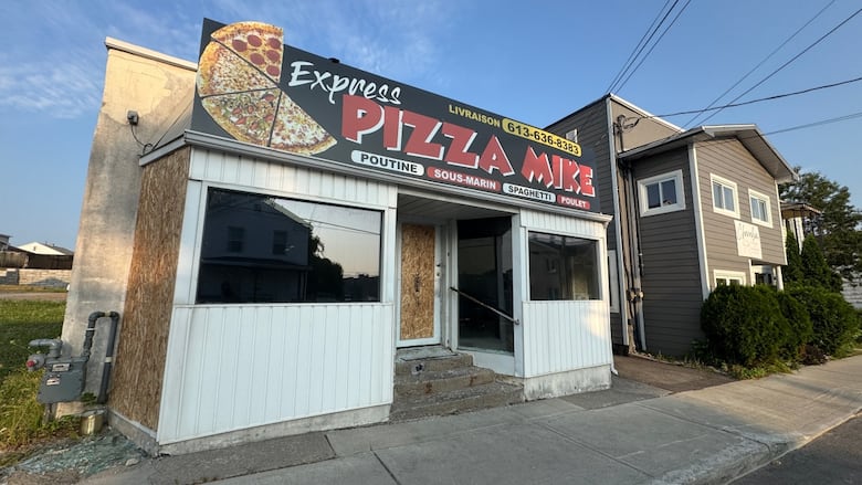 The front of a pizza shop damaged by fire. The door is boarded up.
