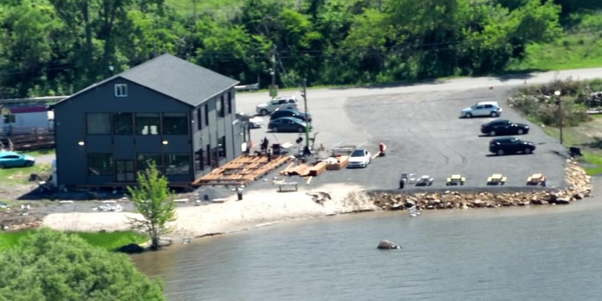 The image shows a building that has property backed out onto the shore of a lake. There are rocks built up along the shore.
