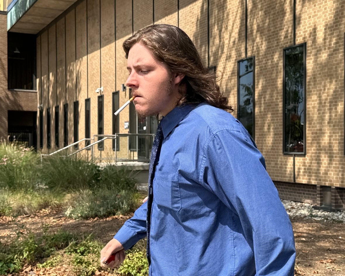 A man with long hair smoking a cigarette leaves a courthouse.