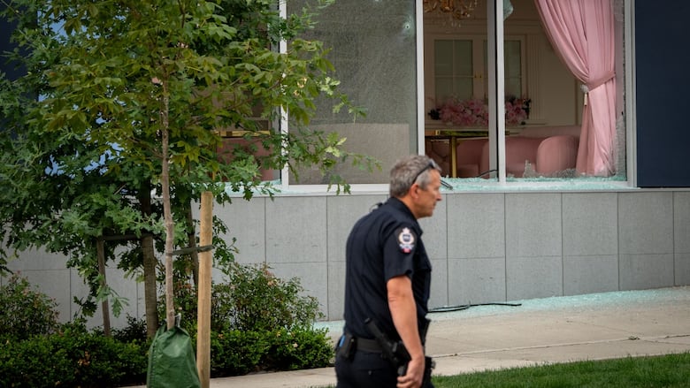 A police officer walks past smashed cafe windows.