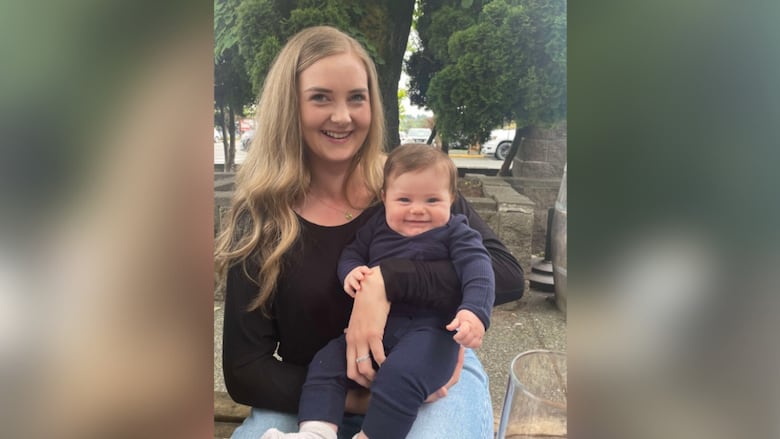 A woman with long blond hair holds a baby. Both are smiling. 