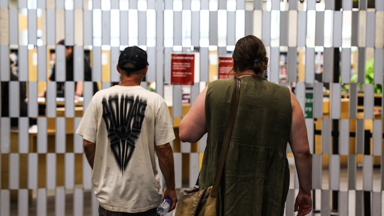 Two men with their backs turned look at a closed gate. 