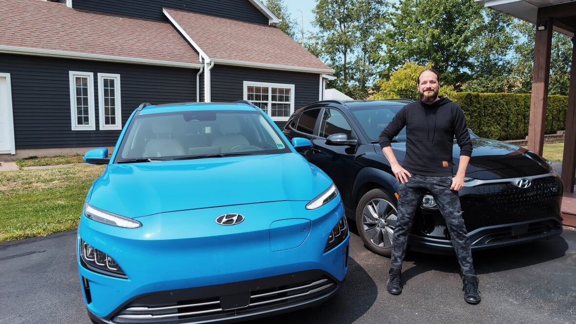 A man standing in-between a blue car and black car of the same model.