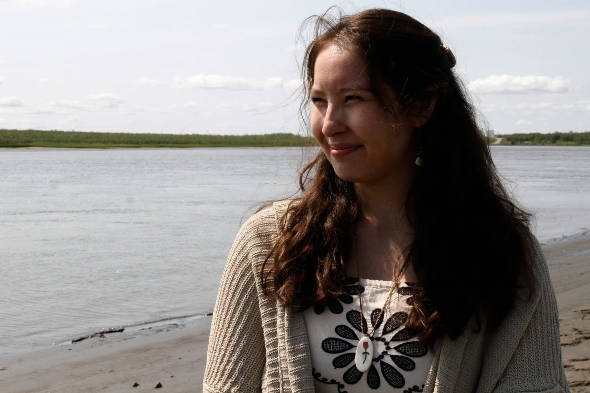 A young woman stands beside a river.