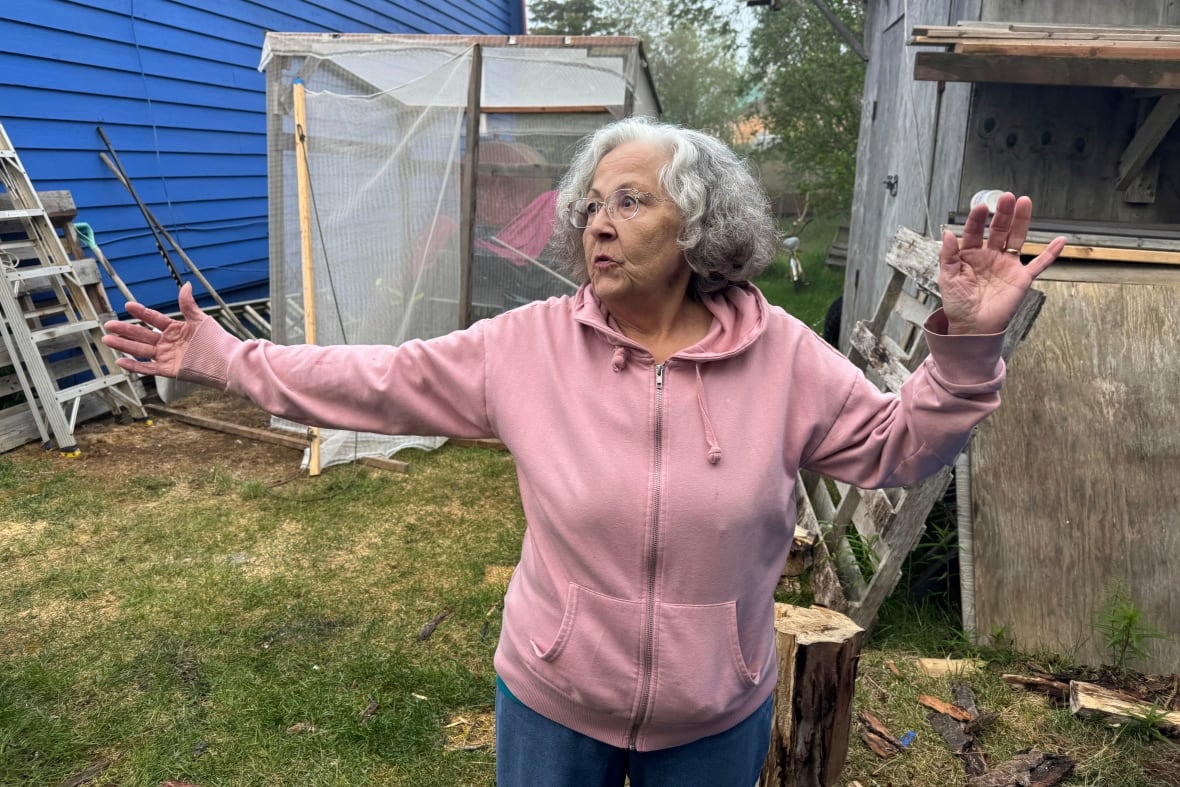 An older woman stands outside a building gesturing as she speaks.