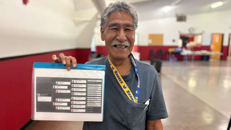 Man with short hair and dark short sleeved shirt holds up a paper with his past relatives names on a family tree.