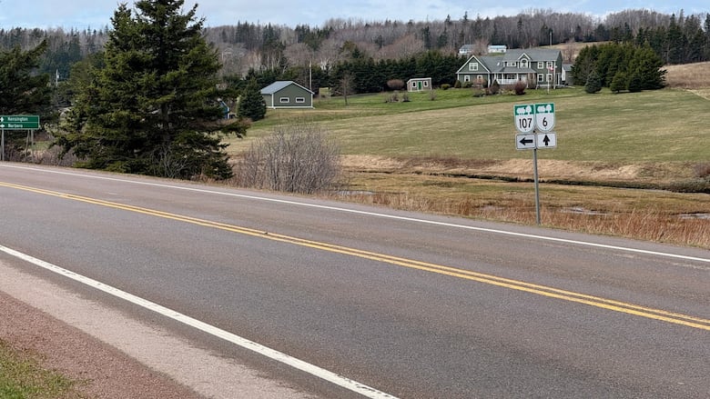 A two lane stretch of road is shown in Clinton, P.E.I. There is a white house in the background and road signs in the foreground. 