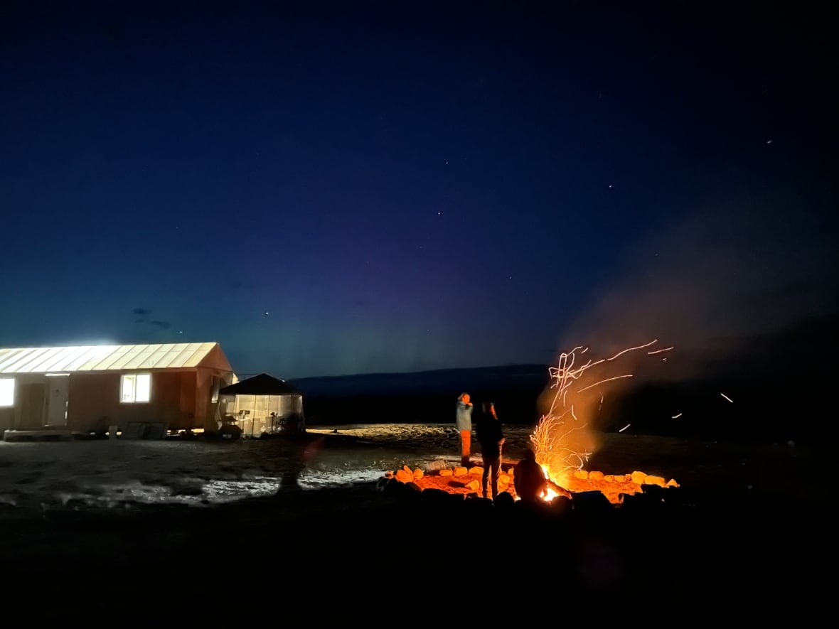 People enjoying a campfire by a Cree made cabin. 