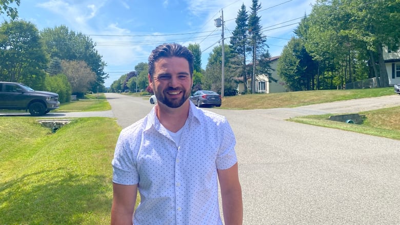A smiling man standing on a quiet tree-lined street.