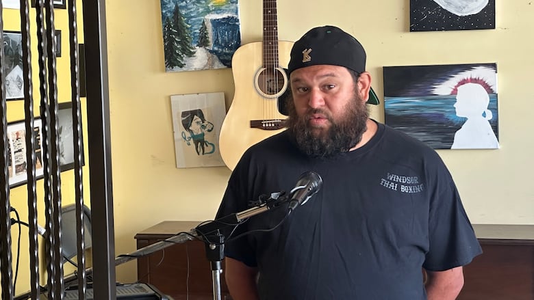 Close up of Michael, in a t-shirt and ball-cap and sporting a bushy beard, speaking at a podium. 
