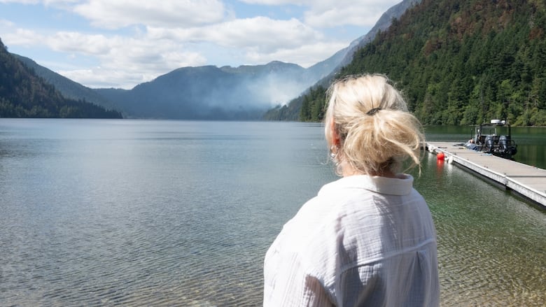 A woman watches a fire across a lake.