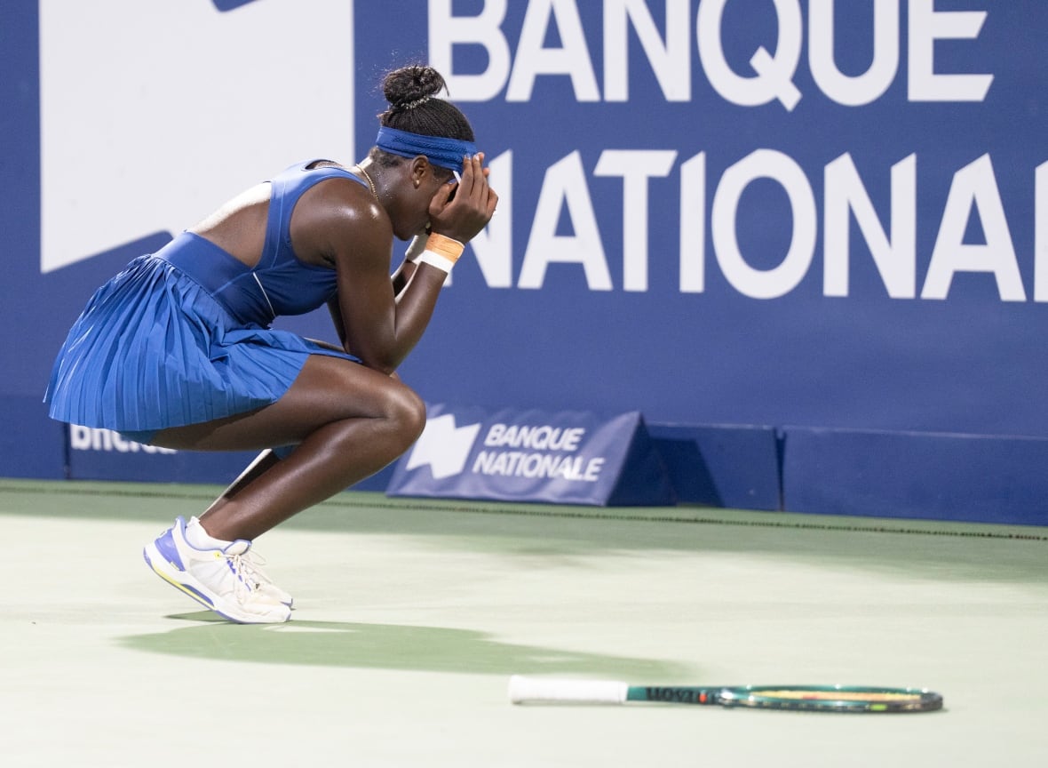 A woman who wears a blue tennis dress and a bullfighting band and hides her face while celebrating on a tennis court where her racket tennis is located. 