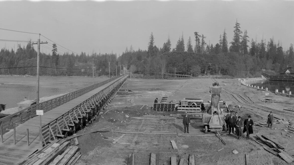 La foto en blanco y negro muestra a los hombres parados cerca de una máquina en un área plana sucia. Hay un largo puente de madera hacia los árboles en el fondo de su derecha. El lado izquierdo de la película la última laguna se roda en el lado izquierdo.