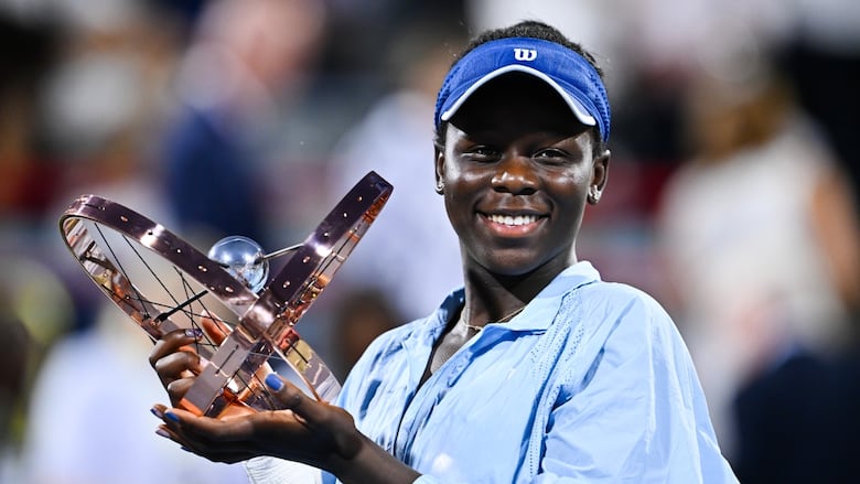 A women's tennis player poses with a trophy.