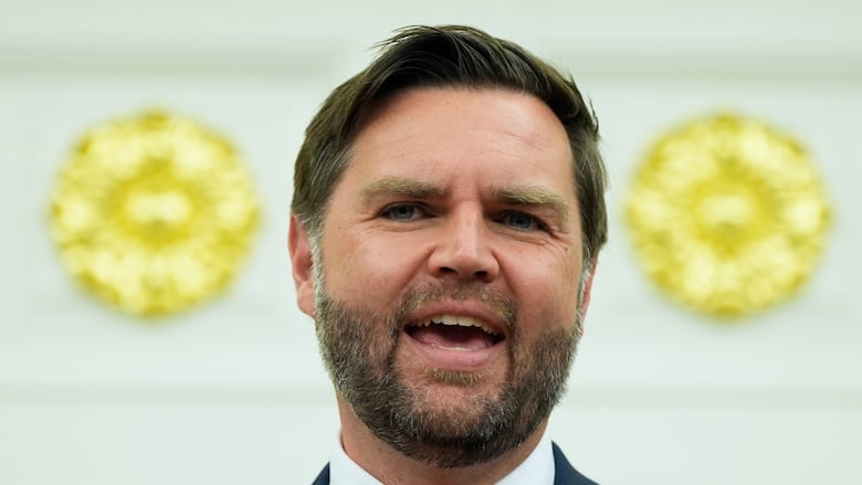 A bearded man in a suit and tie is shown speaking in a closeup photo.