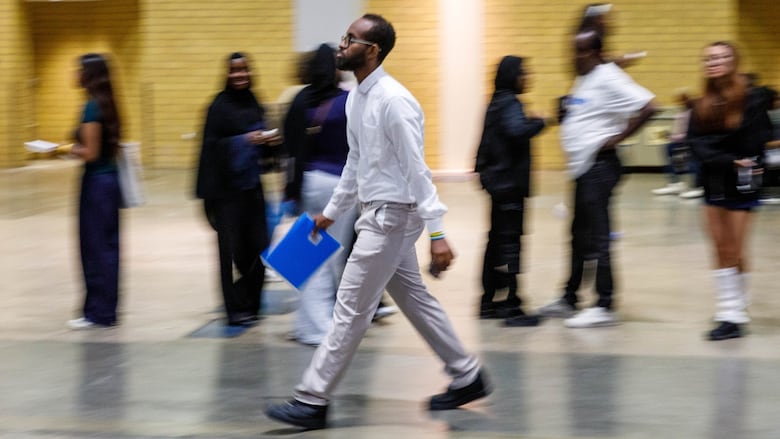 A man walks across a room with a blue folder in hand.