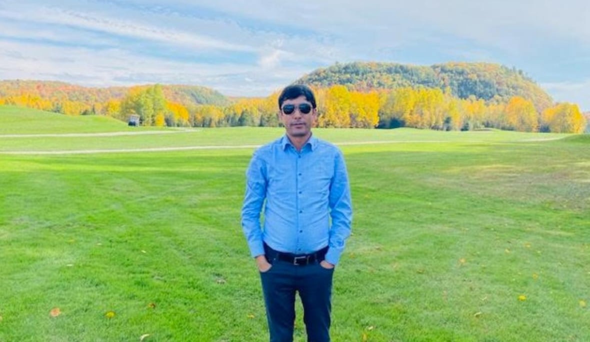 A man with sunglasses standing on green field looks into the camera.