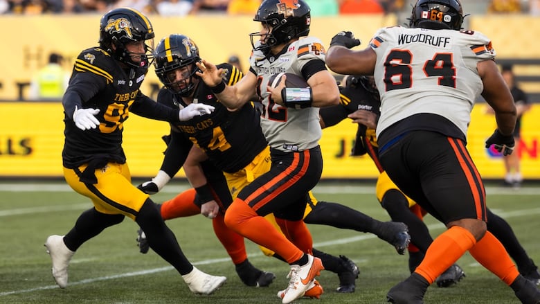 B.C. Lions quarterback Nathan Rourke (12) runs the ball against pressure from Hamilton Tiger-Cats' Julian Howsare (95) during first half CFL football action in Hamilton, on Thursday, August 7, 2025. 