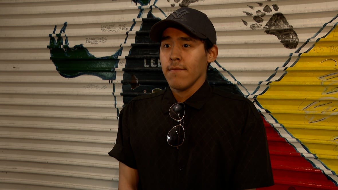 A young man from Nunavut wearing a baseball camp standing next to a painted wall. 
