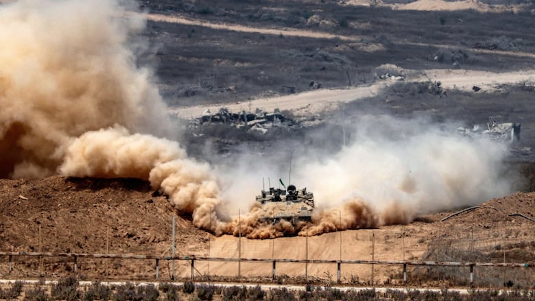 Dust clouds billow around a brown tank as it drives along a dirt road, with scrub brush around it.