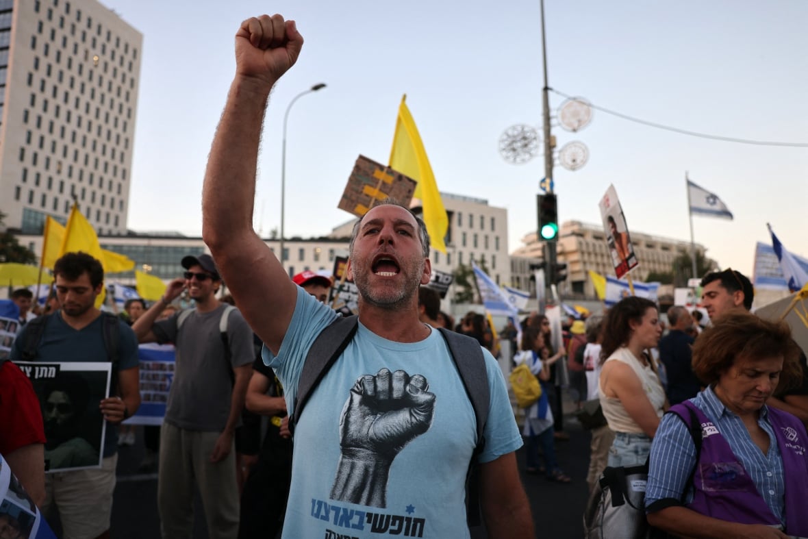A man wearing a light blue T-shirt raises his fist in the air as he shouts, during a demonstration outside.