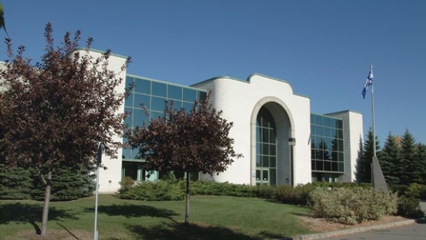 A white building with large windows, with trees and a Quebec flag in front.
