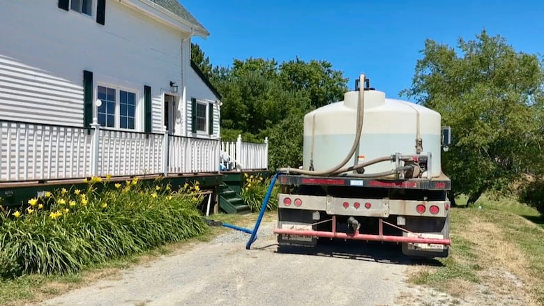 A truck carrying a large tank of water is parked next to a home. 