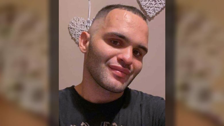 A man in a black T-shirt smiles while looking into the camera lens.