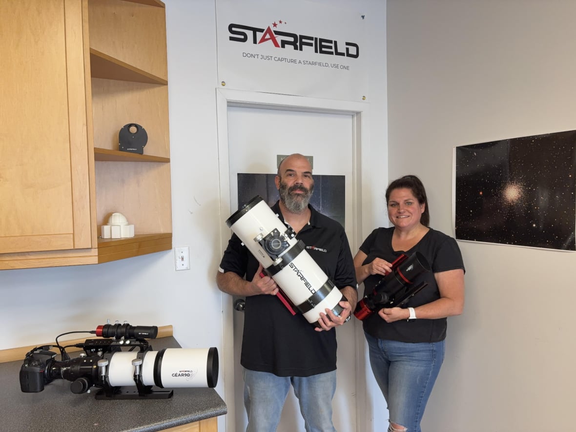 A man holding a white and black telescope is standing next to a woman.