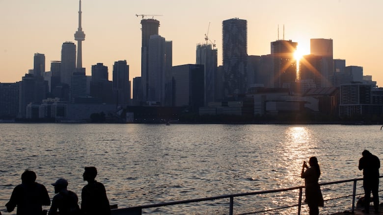The Toronto skyline is seen across the lake while the sun is beaming through the buildings. 