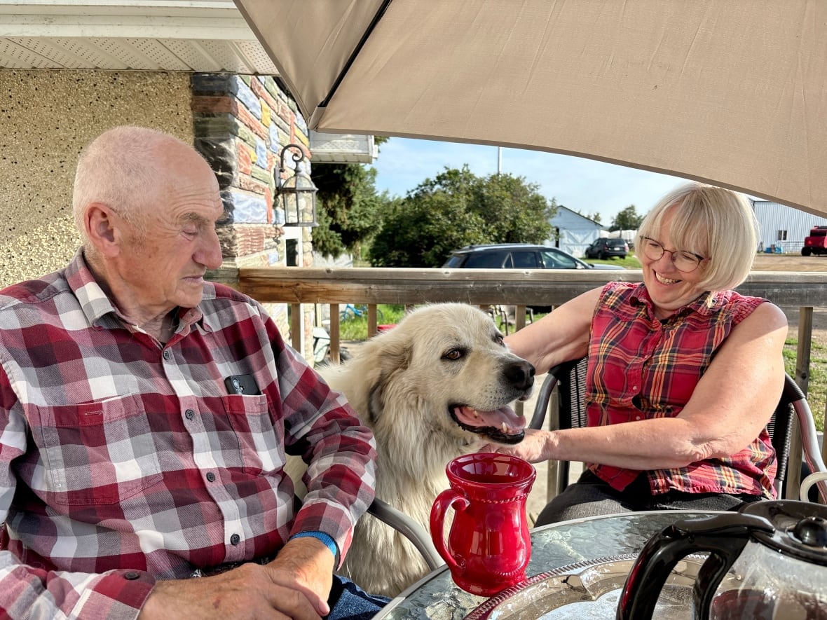 Um homem e uma mulher posam com um grande cachorro branco.