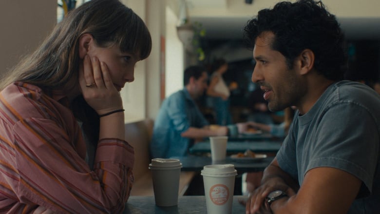 A woman and a man sit across from each other in a coffee shop at a small table, talking.