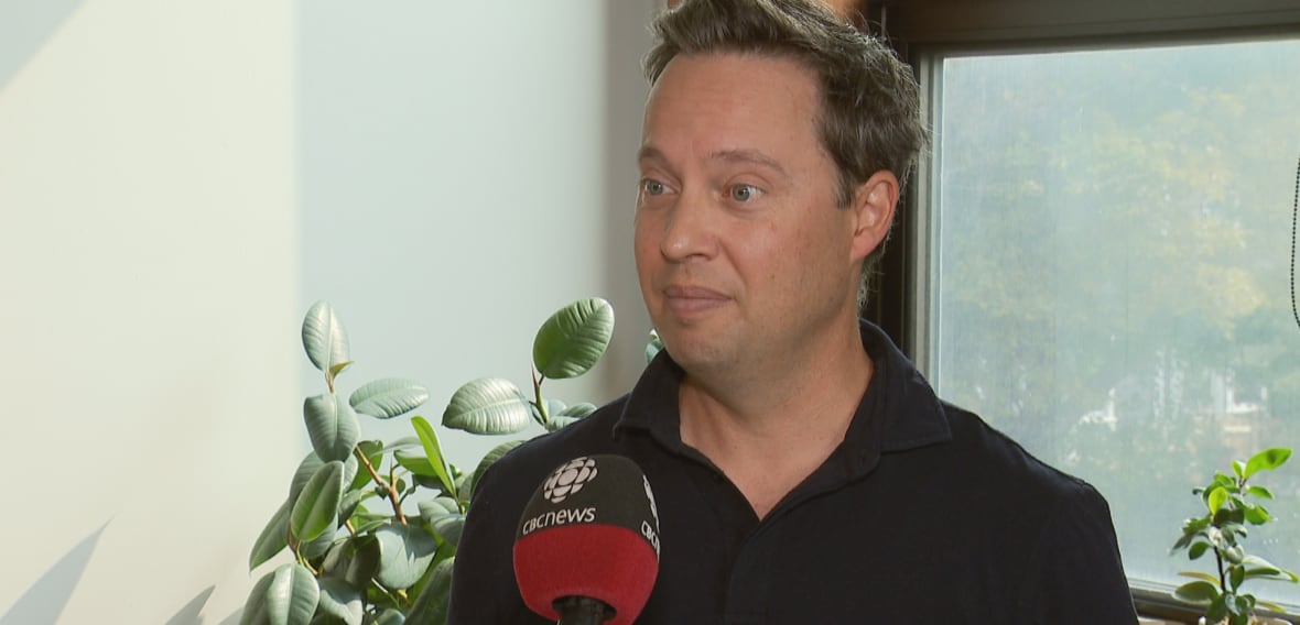 A man in a black shirt, he talks into a CBC News microphone.