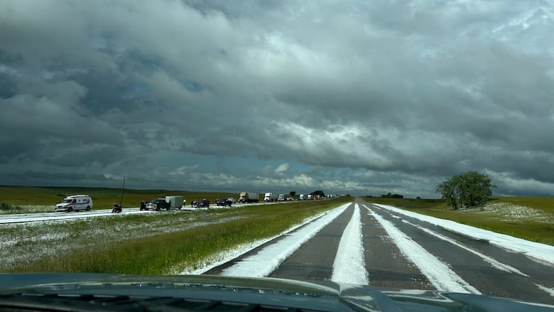 Highway with long white lines of hail. Cars in opposite lane are slowed, lots of clouds in the sky.