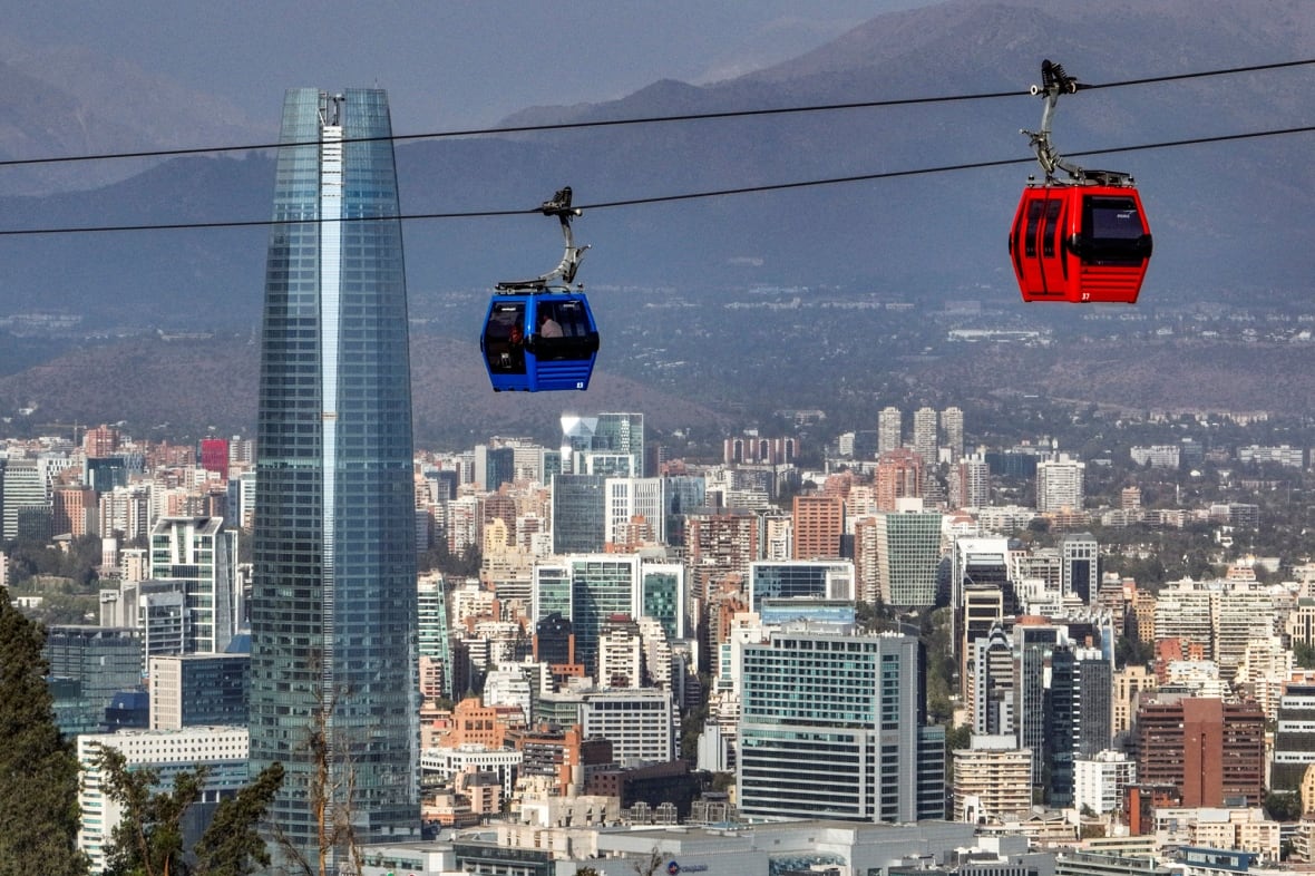 Two cable cars move in the air with a cityscape in the background.