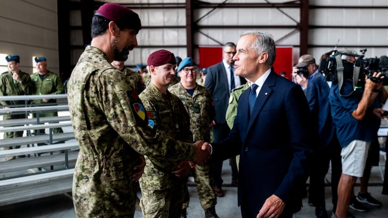 A man in a suit shakes hands with military members.