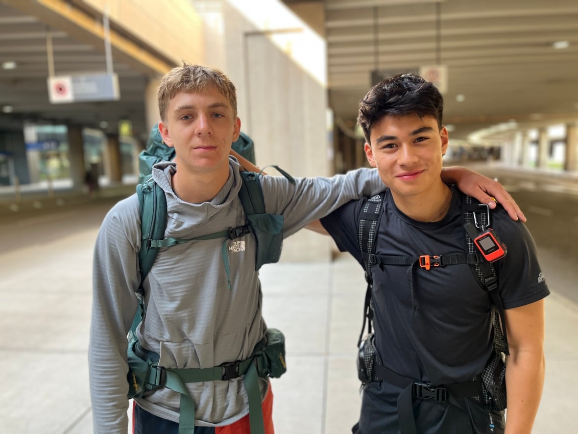Two young men wearing backpacks pose for a photo at the Calgary International Airport.