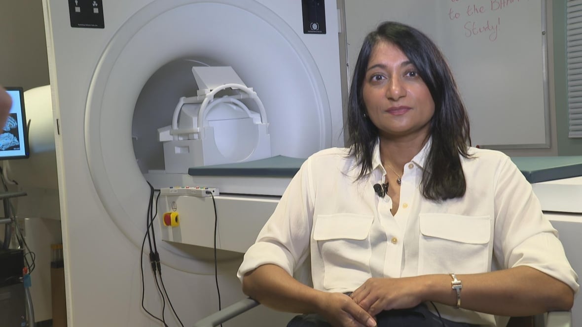 Extra ladies get Alzheimer's than males. It could not simply be as a result of they reside longer 2 A woman with straight black hair stares at the camera with a slight smile. She is wearing a white blouse and a silver watch. There's an MRI machine behind her.