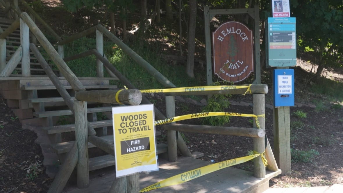 Entrance to a path with yellow tape on him and sign saying "Trail closed to travel, fire danger."