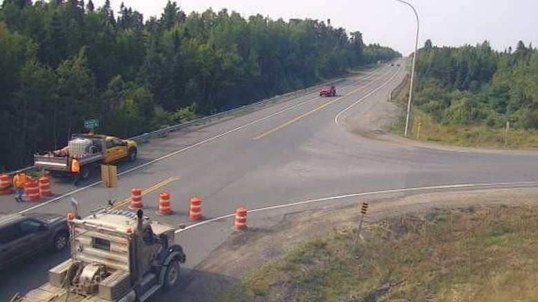 A intersection on a highway is blocked by trucks and pylons.