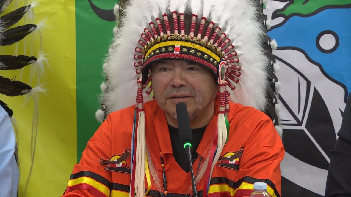 Man wearing feathered headdress and orange shirt 